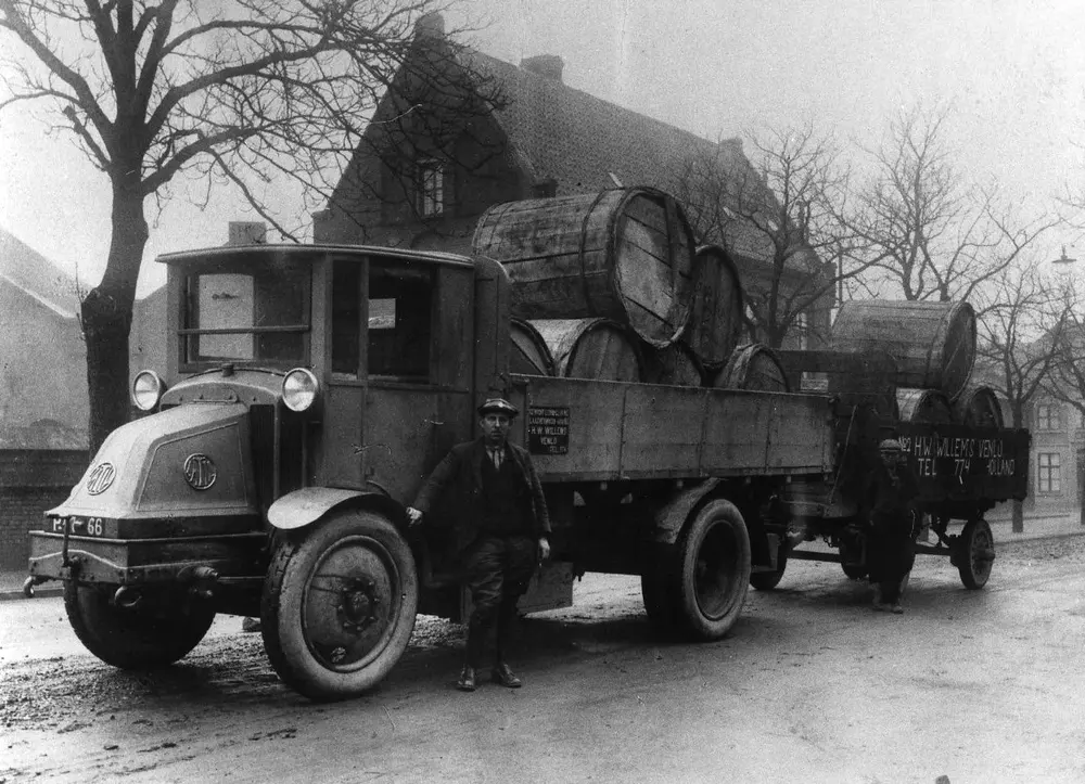 A 1920s truck and trailer loaded with barrels, with two men beside it, on a street in Venlo.